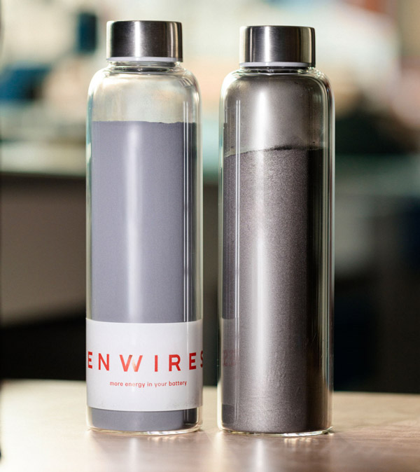 Two glass bottles side by side: raw graphite powder on the left, darker SiBoost silicon-doped powder on the right, both labelled Enwires