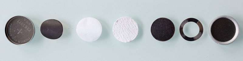 Coin cell components laid out in a row: case, electrode discs, separator, spring, spacer and cap