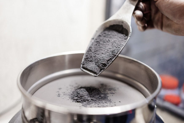 A scoop of graphite powder being measured and added into a mixing vessel